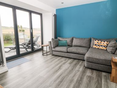 A living room with a sectional sofa and glass sliding doors opening to an outdoor area at Atlantic Reach in Widemouth Bay