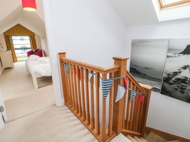 A staircase with wooden railing and bunting leading to a bedroom with bed pink chair and yellow curtains at Atlantic Reach in Widemouth Bay