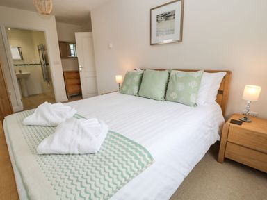 A bedroom with a bed with green pillows white towels on a blanket and a bedside table with a lamp at Atlantic Reach in Widemouth Bay