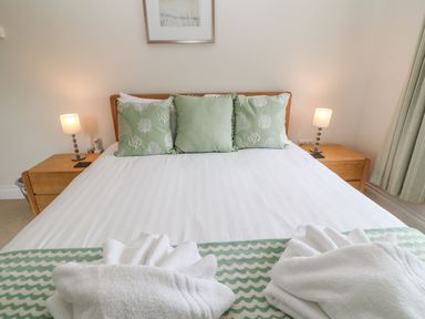 A bedroom with a bed with green pillows and white towels on a blanket at Atlantic Reach in Widemouth Bay