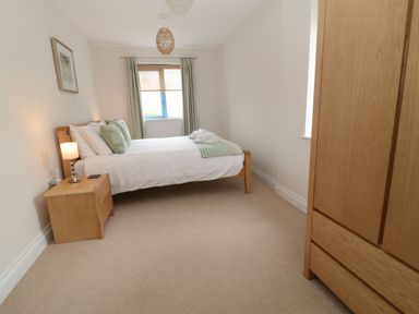 A bedroom with a wooden bed with white and green bedding a wooden bedside table with a lamp and a wooden wardrobe at Atlantic Reach in Widemouth Bay