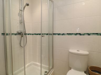 A bathroom with a corner shower enclosure and a toilet next to a woven basket at Atlantic Reach in Widemouth Bay