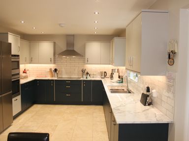 A kitchen with white and dark cabinets a stainless steel refrigerator and oven a marble countertop and tiled walls at Atlantic Reach in Widemouth Bay