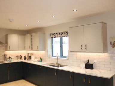 A kitchen with dark lower cabinets and light upper cabinets with a window over the sink at Atlantic Reach in Widemouth Bay