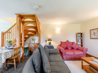 A living room with sofas wooden staircase dining table and bookshelf at Cwmdu Cottage in Cwm-Cou near Newcastle Emlyn