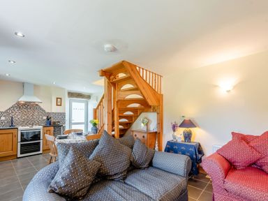 A living room and kitchen with blue and red couches wooden dining table and stairs at Cwmdu Cottage in Cwm-Cou near Newcastle Emlyn