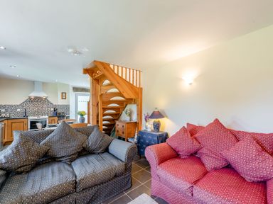 A living room with two sofas and a wooden staircase next to a kitchen at Cwmdu Cottage in Cwm-Cou near Newcastle Emlyn