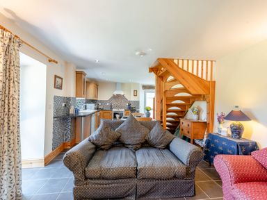 An open-plan living room and kitchen area with a patterned sofa wooden staircase and tiled floor at Cwmdu Cottage in Cwm-Cou near Newcastle Emlyn