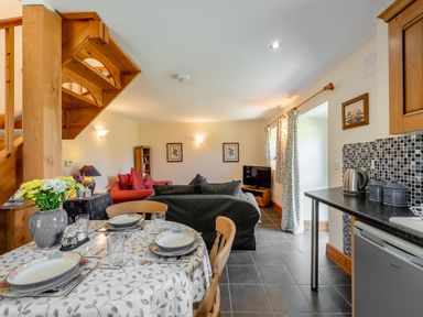 A dining table set with plates and glasses near a living room with sofas and a television at Cwmdu Cottage in Cwm-Cou near Newcastle Emlyn