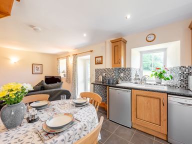 A kitchen and dining area with a round table set for four and a view of a living room at Cwmdu Cottage in Cwm-Cou near Newcastle Emlyn