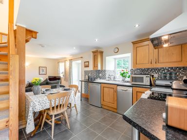 A kitchen and dining area with wooden cabinets a tiled floor a dining table with chairs and a window at Cwmdu Cottage in Cwm-Cou near Newcastle Emlyn