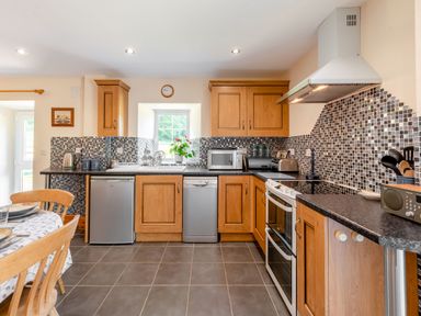 A kitchen with wooden cabinets a tiled backsplash appliances and a dining table at Cwmdu Cottage in Cwm-Cou near Newcastle Emlyn