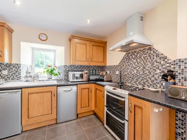 A kitchen with wooden cabinets silver appliances mosaic tile backsplash and a window with a plant at Cwmdu Cottage in Cwm-Cou near Newcastle Emlyn