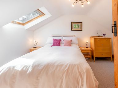 A bedroom with a bed a skylight window two bedside tables and a dresser at Cwmdu Cottage in Cwm-Cou near Newcastle Emlyn