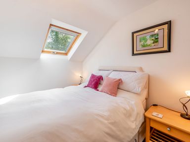 A bedroom with a double bed with white bedding and two pink pillows under a skylight window at Cwmdu Cottage in Cwm-Cou near Newcastle Emlyn