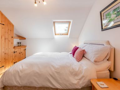 A bedroom with a double bed white bedding and purple pillows a wooden wardrobe a skylight window and a bedside table with a coaster at Cwmdu Cottage in Cwm-Cou near Newcastle Emlyn