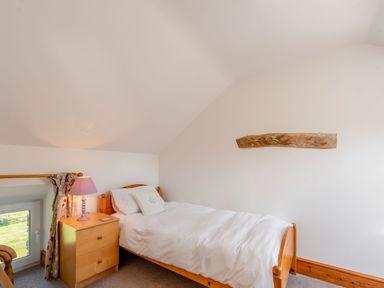 A bedroom with a single bed next to a wooden nightstand and a small window at Cwmdu Cottage in Cwm-Cou near Newcastle Emlyn