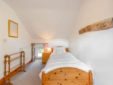 A bedroom with a single wooden bed a wooden nightstand with a lamp a mirror and a window at Cwmdu Cottage in Cwm-Cou near Newcastle Emlyn