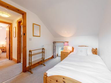 A small bedroom with a single bed bedside table and lamp visible through an open door at Cwmdu Cottage in Cwm-Cou near Newcastle Emlyn