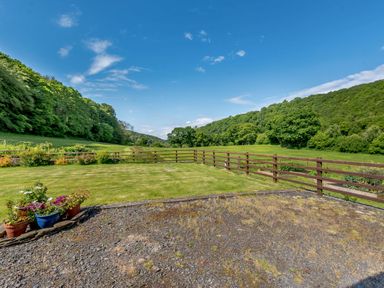 A fenced grassy yard with potted plants and trees on hills in the background at Cwmdu Cottage in Cwm-Cou near Newcastle Emlyn