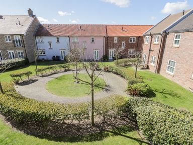 A courtyard with a circular paved path surrounded by grass trees and hedges between brick and painted residential buildings at Sunny Bay The Bay near Filey