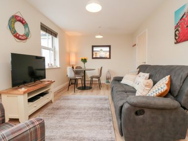 A living room with a gray sofa and dining table with chairs at Sunny Bay in The Bay near Filey