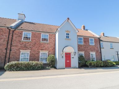A two story brick house with a red door bushes and windows at Sunny Bay The Bay near Filey