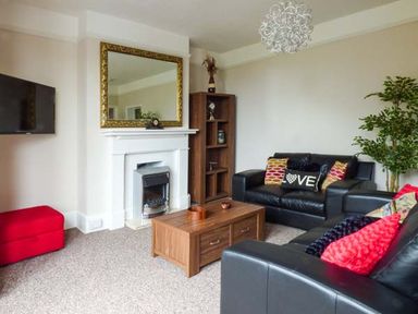 A living room with black leather sofas a wooden coffee table a white fireplace with a gold framed mirror and a wall mounted TV at Westgate Retreat in Hunstanton