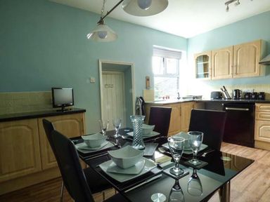 A kitchen with a black dining table set with bowls and glasses and light wood cabinets at Westgate Retreat in Hunstanton