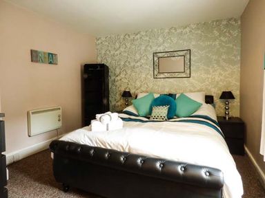 A bedroom with a large bed with pillows and towels a black cabinet two bedside tables with lamps and a wall mirror at Westgate Retreat in Hunstanton