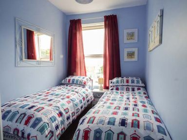 A bedroom with two single beds with patterned bedding and a window with red curtains at Westgate Retreat in Hunstanton