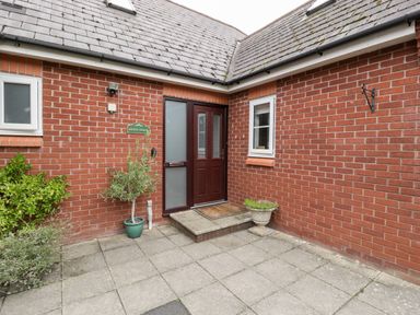 A brick exterior entrance with a dark wooden door two small windows and potted plants at Hurst Green in Ewyas Harold near Hereford