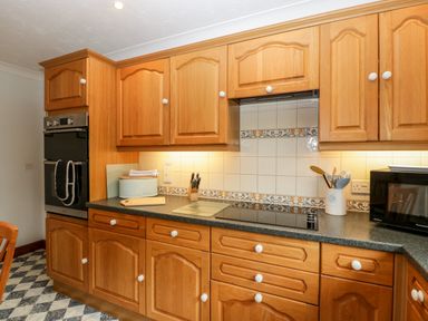 A kitchen with wooden cabinets a built in oven a stovetop a microwave and kitchen utensils at Hurst Green in Ewyas Harold near Hereford