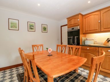 A kitchen with wooden table and chairs a flower in a vase on the table wooden cabinets and a built in oven at Hurst Green in Ewyas Harold near Hereford
