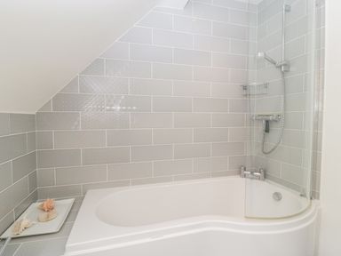 A bathroom with a bathtub shower and gray tiled walls at Hurst Green in Ewyas Harold near Hereford