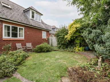 A garden with lawn chairs shrubs and trees next to a brick house at Hurst Green in Ewyas Harold near Hereford