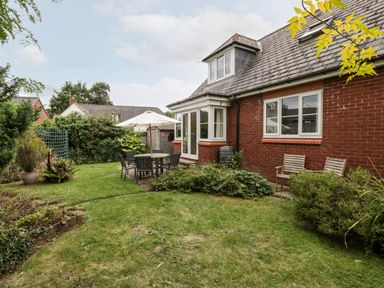 A backyard with a patio table umbrella chairs two wooden chairs plants and shrubs at Hurst Green in Ewyas Harold near Hereford