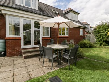A backyard patio with a round table and umbrella surrounded by six chairs at Hurst Green in Ewyas Harold near Hereford