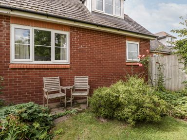 A garden area with two wooden chairs and a small table next to a brick house with windows at Hurst Green in Ewyas Harold near Hereford
