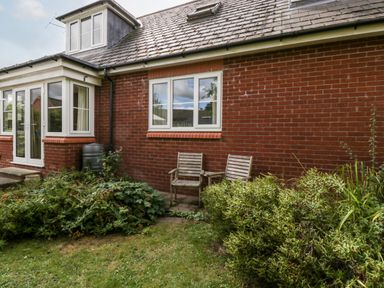 A garden area with two wooden chairs against a red brick house wall at Hurst Green in Ewyas Harold near Hereford