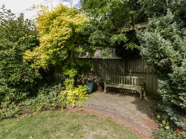 A garden seating area with a wooden bench under a wooden pergola covered with climbing plants and surrounded by shrubs at Hurst Green in Ewyas Harold near Hereford