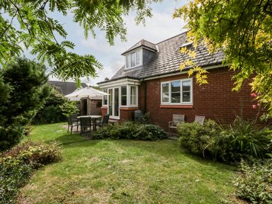 A garden with outdoor table and chairs under an umbrella by a brick house at Hurst Green in Ewyas Harold near Hereford