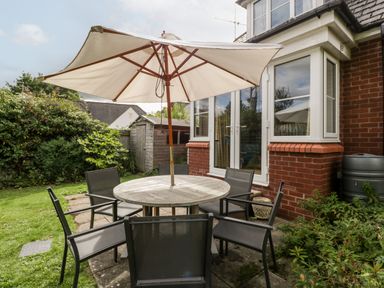A garden patio with a round wooden table, six black chairs, a large white umbrella, and a wooden shed at Hurst Green in Ewyas Harold near Hereford