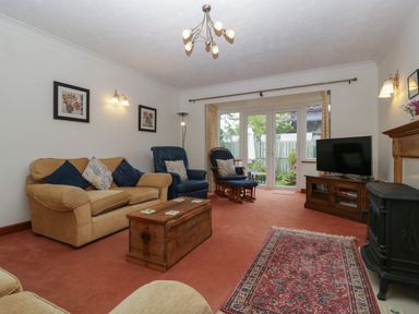 A living room with sofas, a wooden chest table, a rocking chair, a TV on a wooden stand, and glass doors leading outside at Hurst Green in Ewyas Harold near Hereford