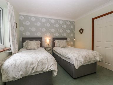 A bedroom with two single beds a nightstand with a lamp between them floral wallpaper and a closed door at Hurst Green Ewyas Harold near Hereford