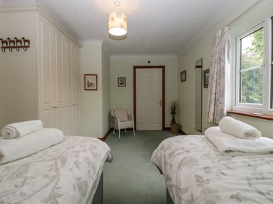 A bedroom with two single beds with white and floral bedding towels on beds a chair a door built in wardrobes and a window with curtains at Hurst Green Ewyas Harold near Hereford