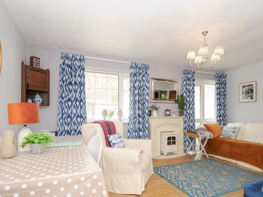 A living room with blue patterned curtains a polka dot tablecloth and a white armchair at No 1 The Heathers Rosecraddoc Lodge near Liskeard