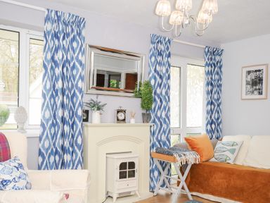 A living room with blue patterned curtains a cream fireplace and sofa with cushions at No 1 The Heathers Rosecraddoc Lodge near Liskeard