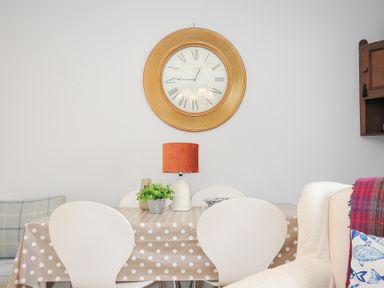 A dining area with a polka dot tablecloth on a table white chairs a wall clock and a lamp at No 1 The Heathers Rosecraddoc Lodge near Liskeard