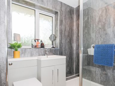 A bathroom with a sink vanity unit a toilet a window with toiletries a small plant and a shower with a blue towel at No 1 The Heathers Rosecraddoc Lodge near Liskeard